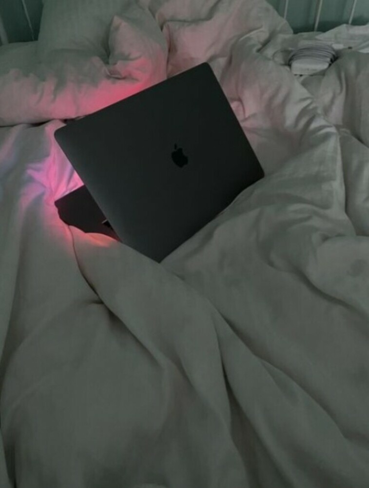 Laptop's light shining pink on the white covers of the bed.